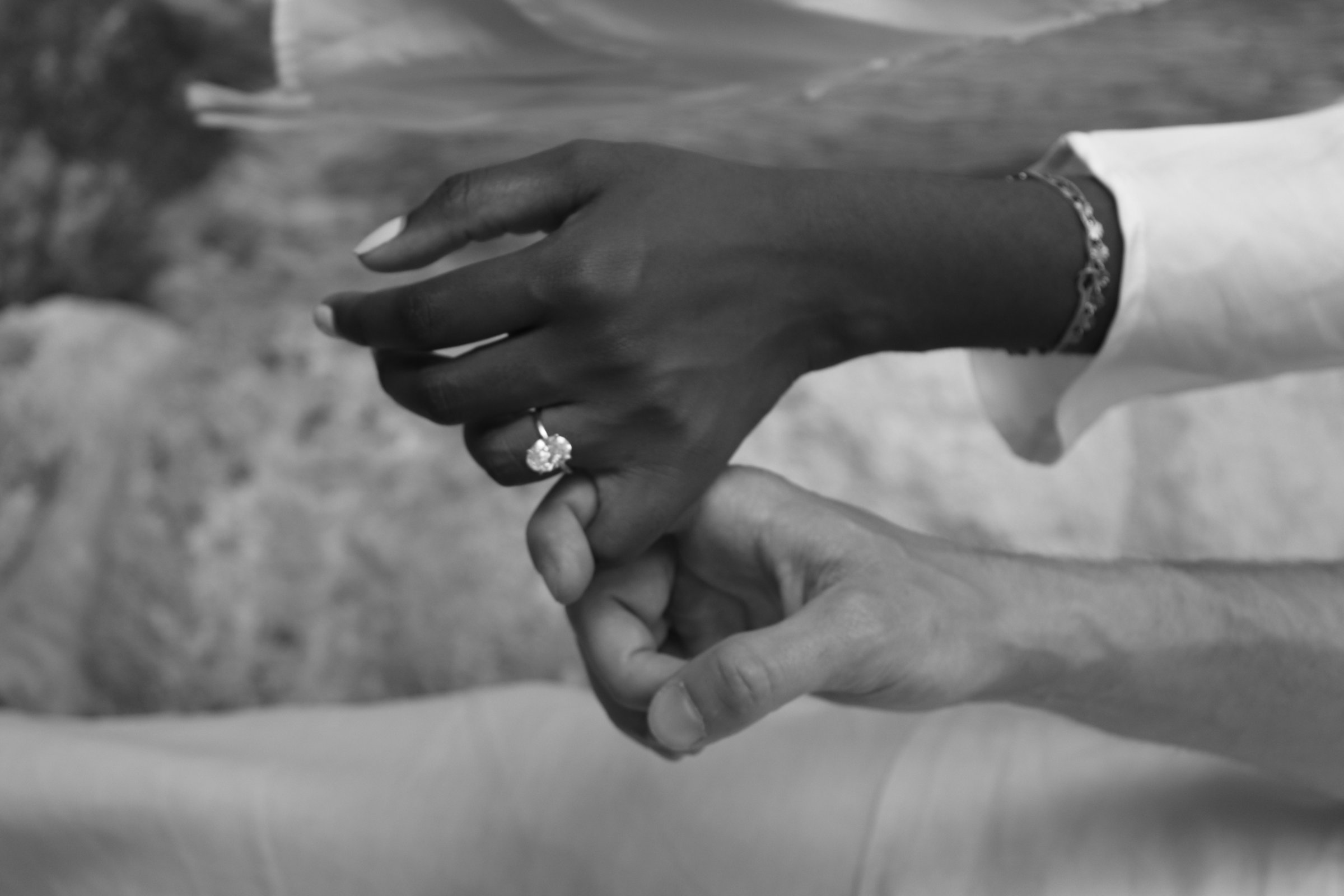 Black and white close-up of Jakob and Sonia holding hands, her engagement ring visible.